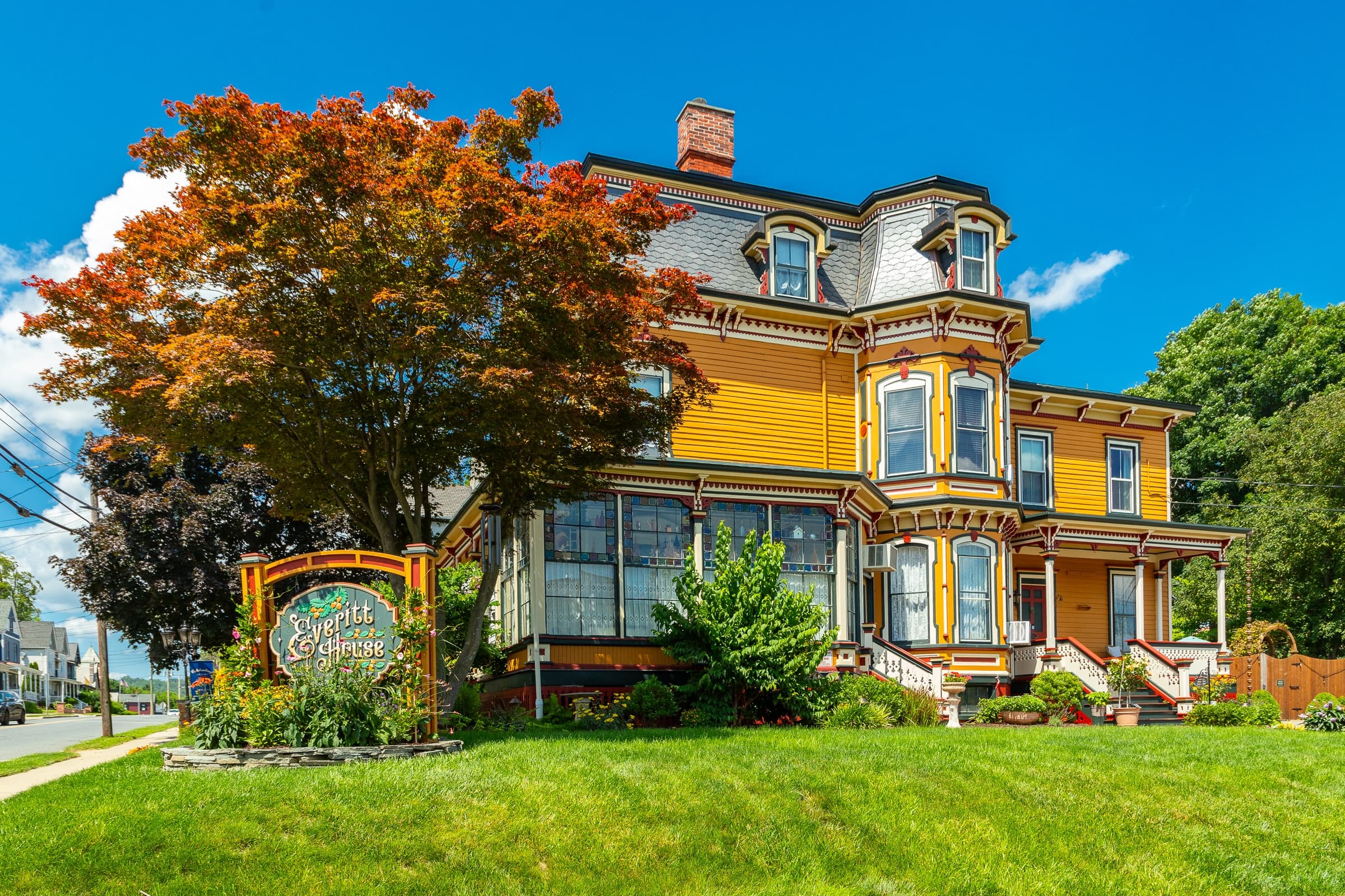A yellow Victorian style house with a tree in front.