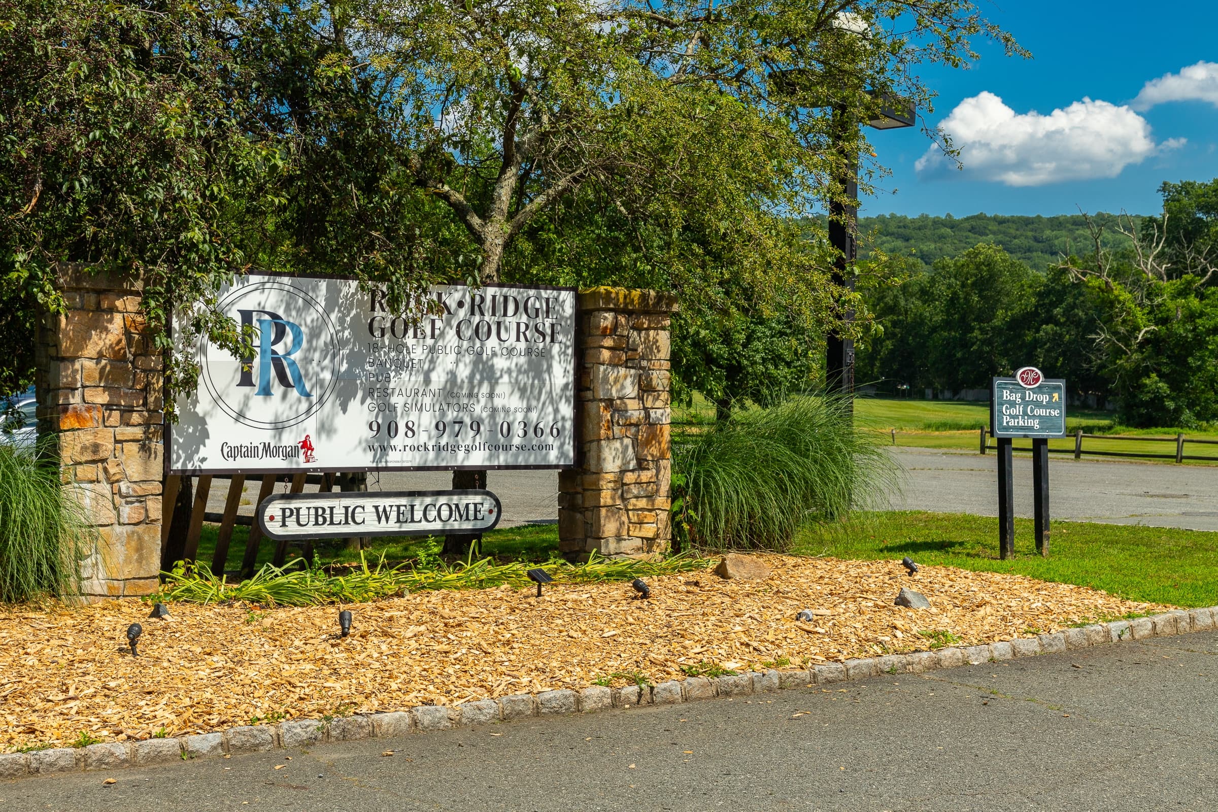 A sign for a public golf course with a phone number and a stop sign in the background.