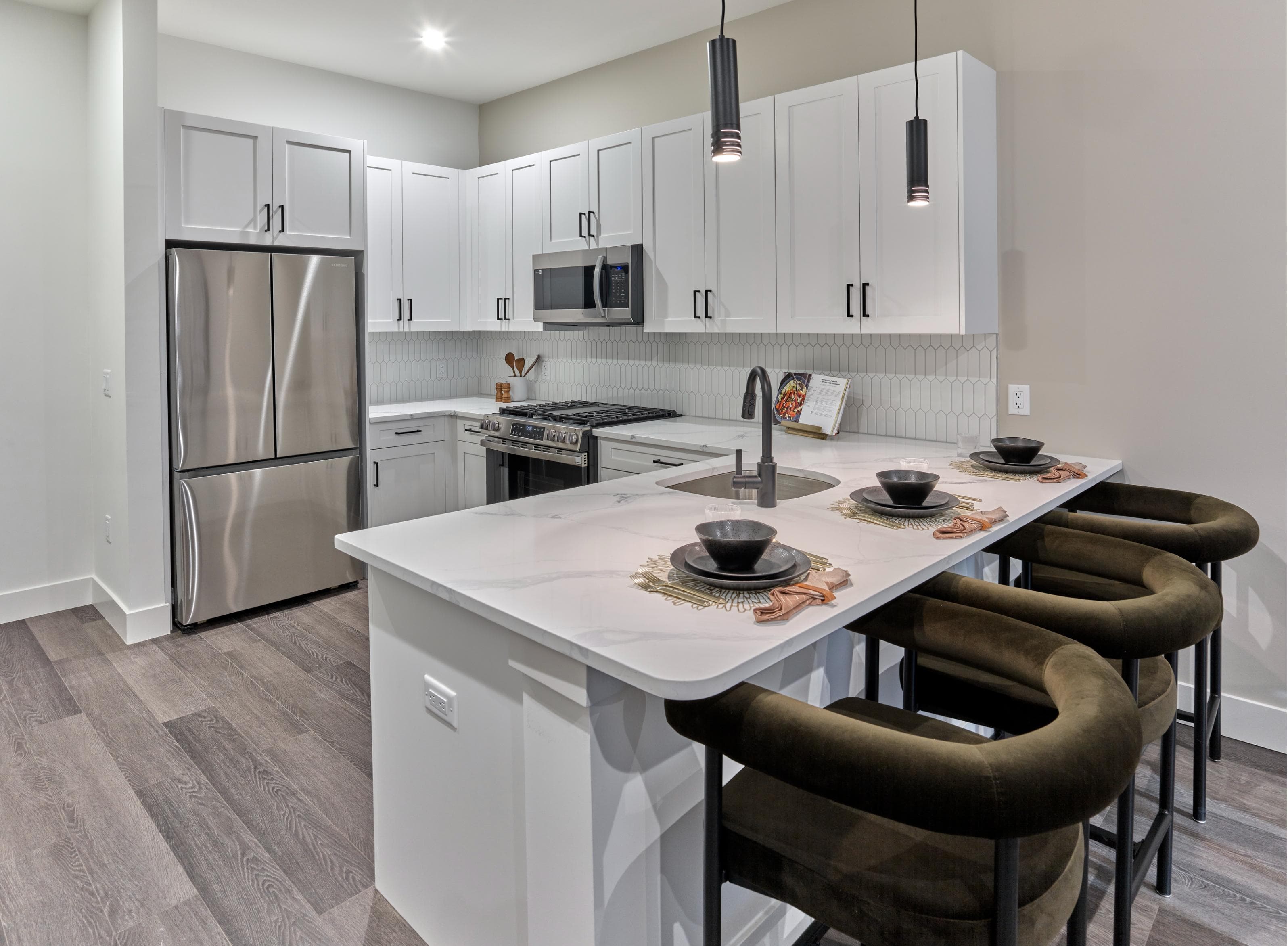 A modern kitchen with a white island and brown chairs.