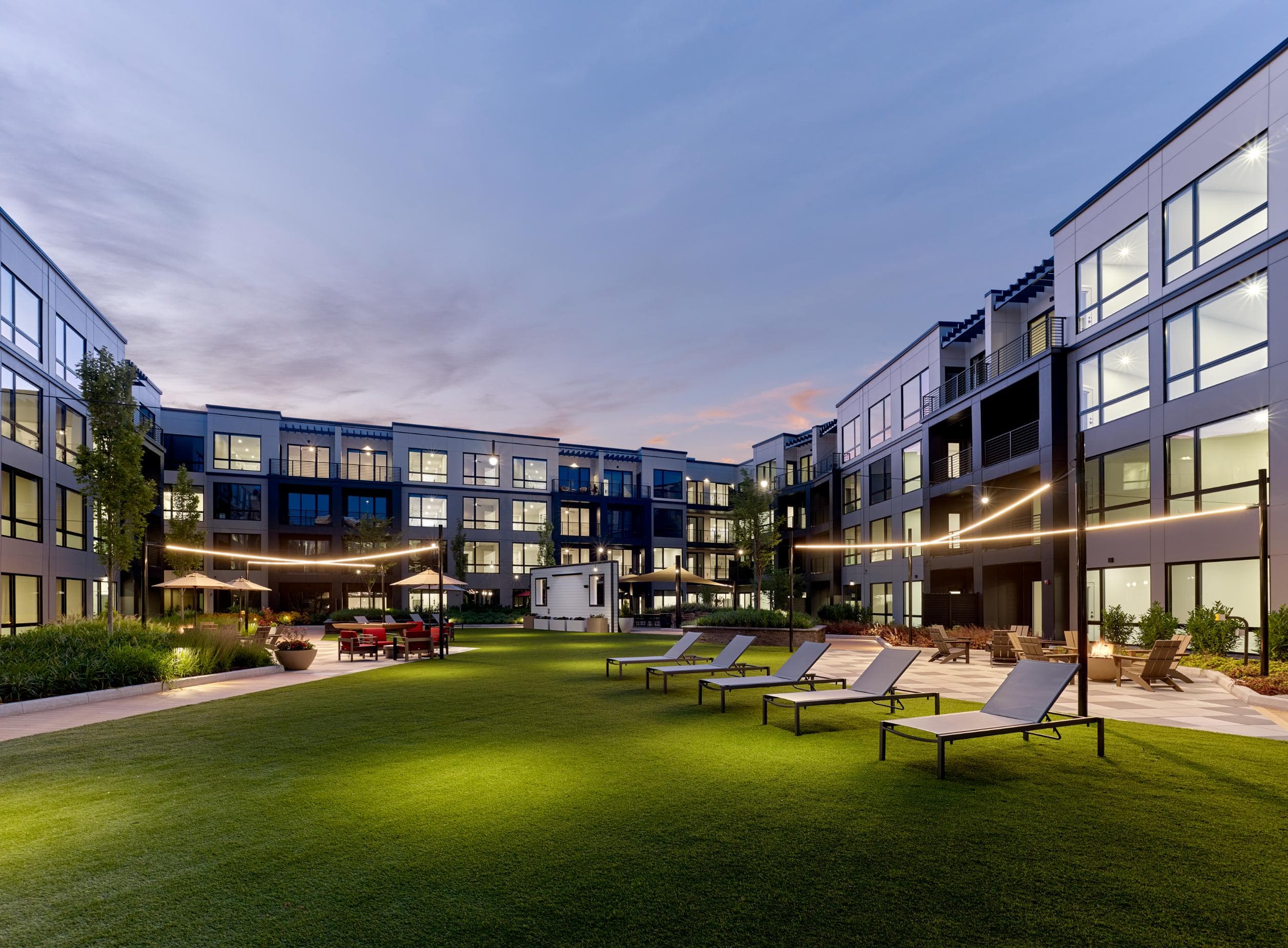 A modern building complex with a grassy area in front and several lounge chairs.