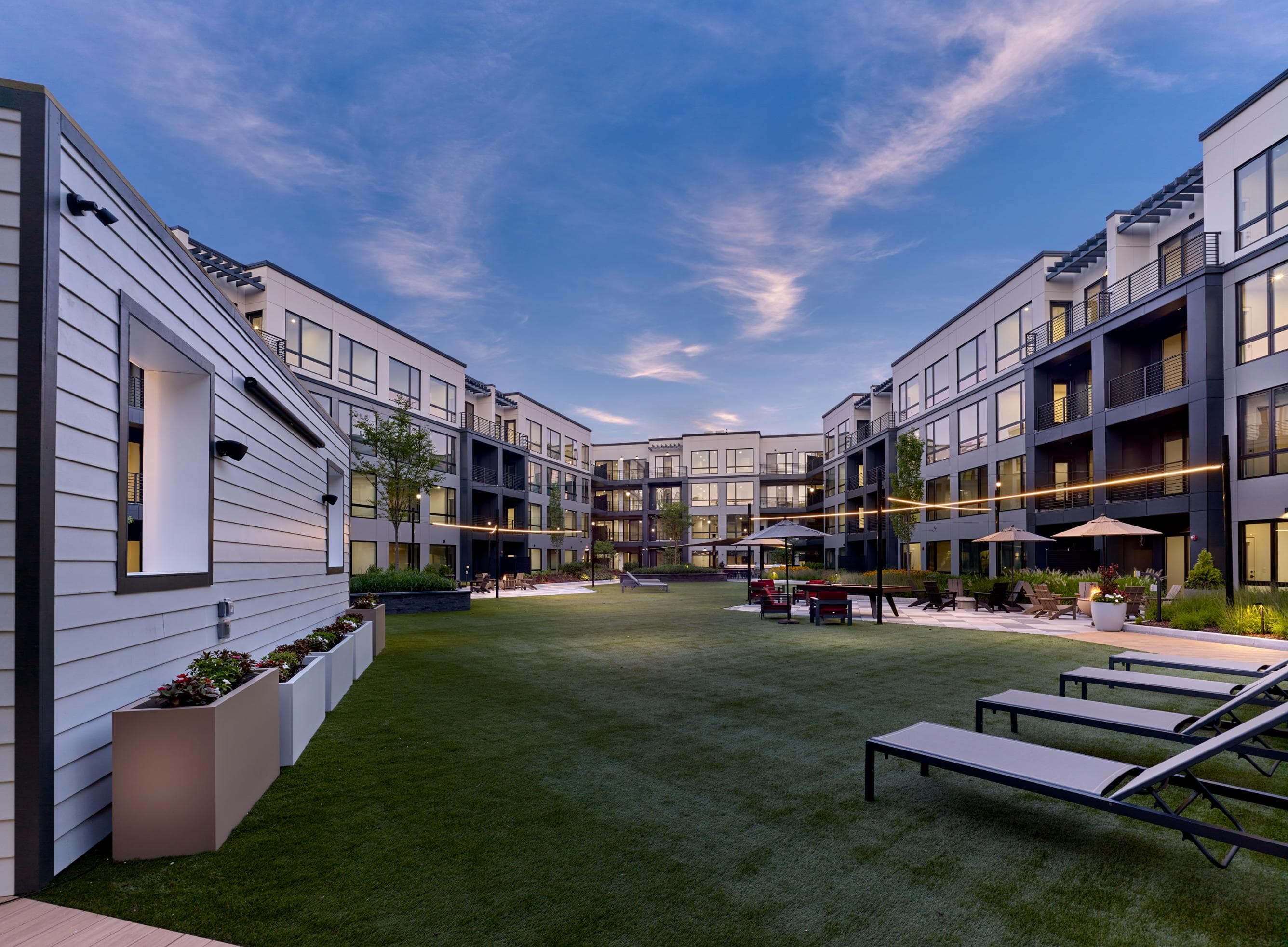 A modern apartment complex with a grassy courtyard and benches.