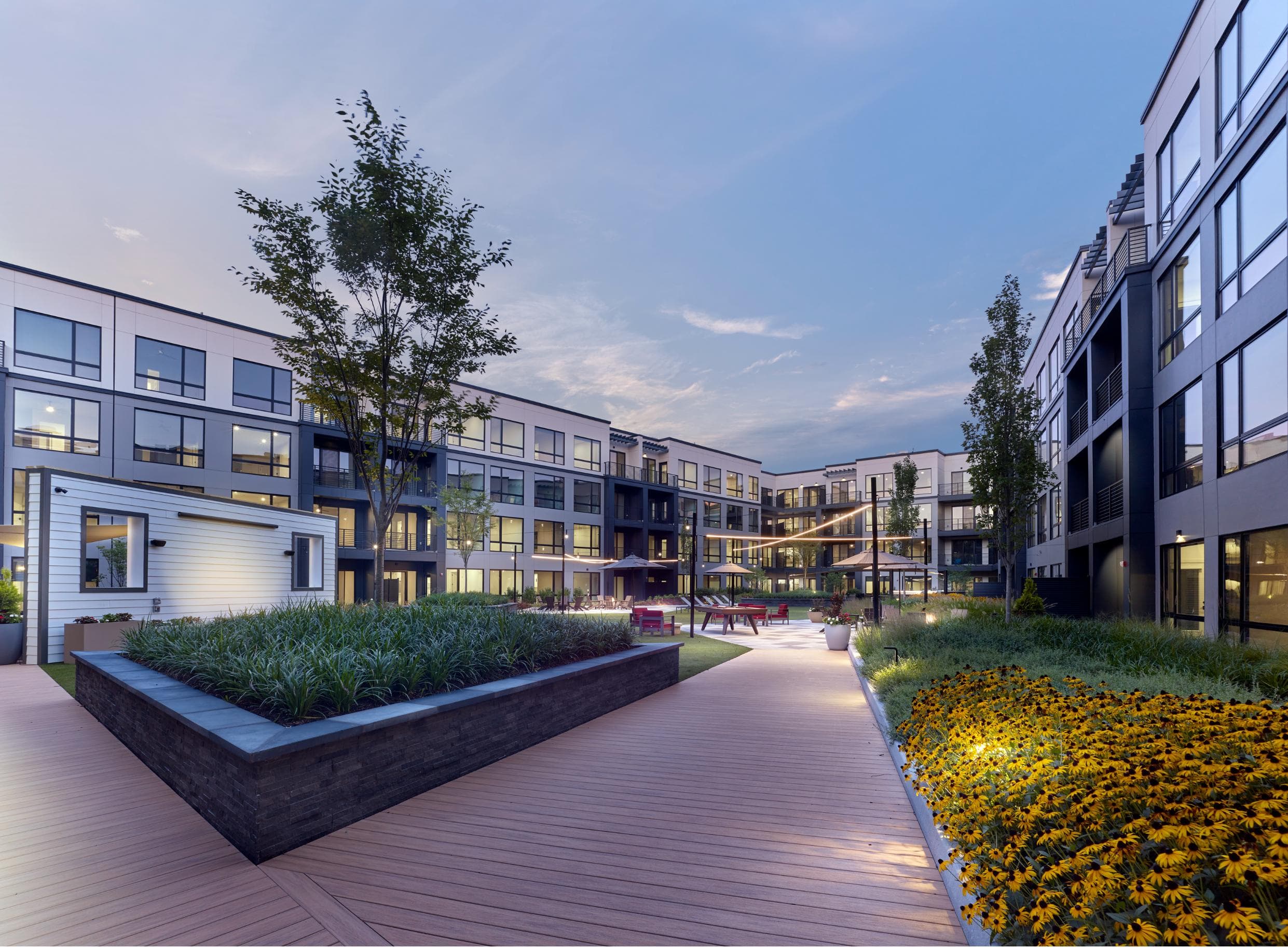 A modern building complex with a wooden walkway and flower beds.