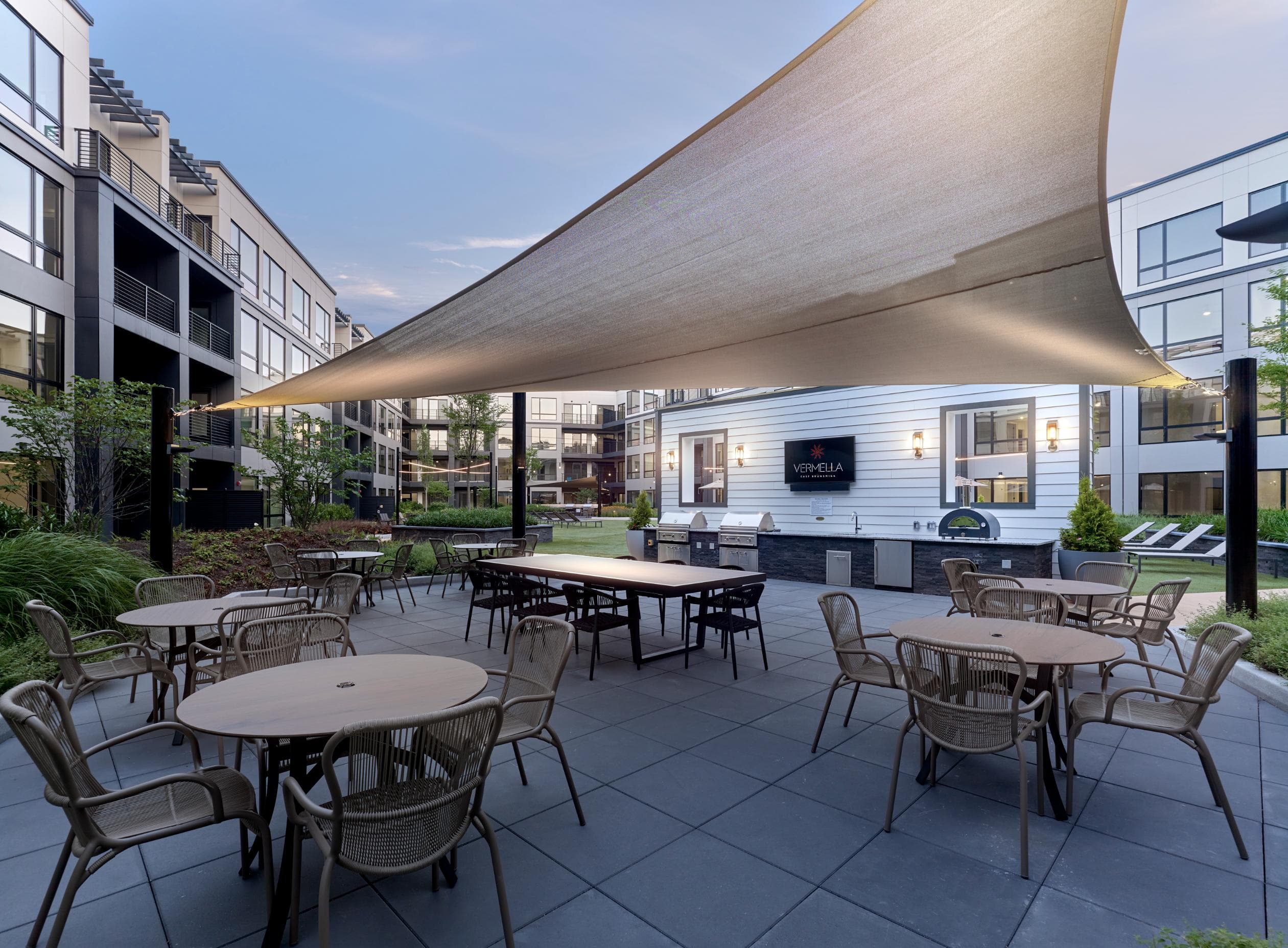 A patio with tables and chairs under a large shade structure.
