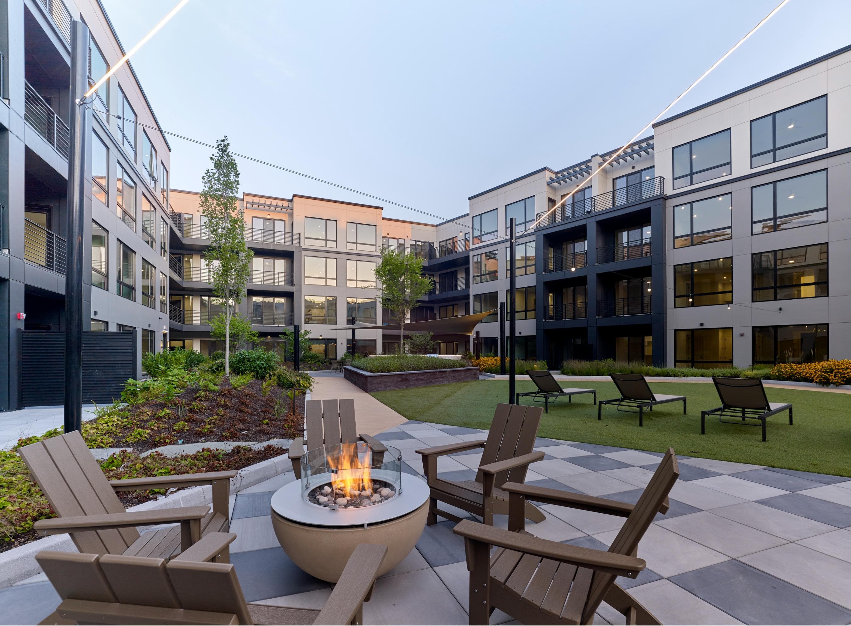A modern courtyard with a fire pit and chairs.