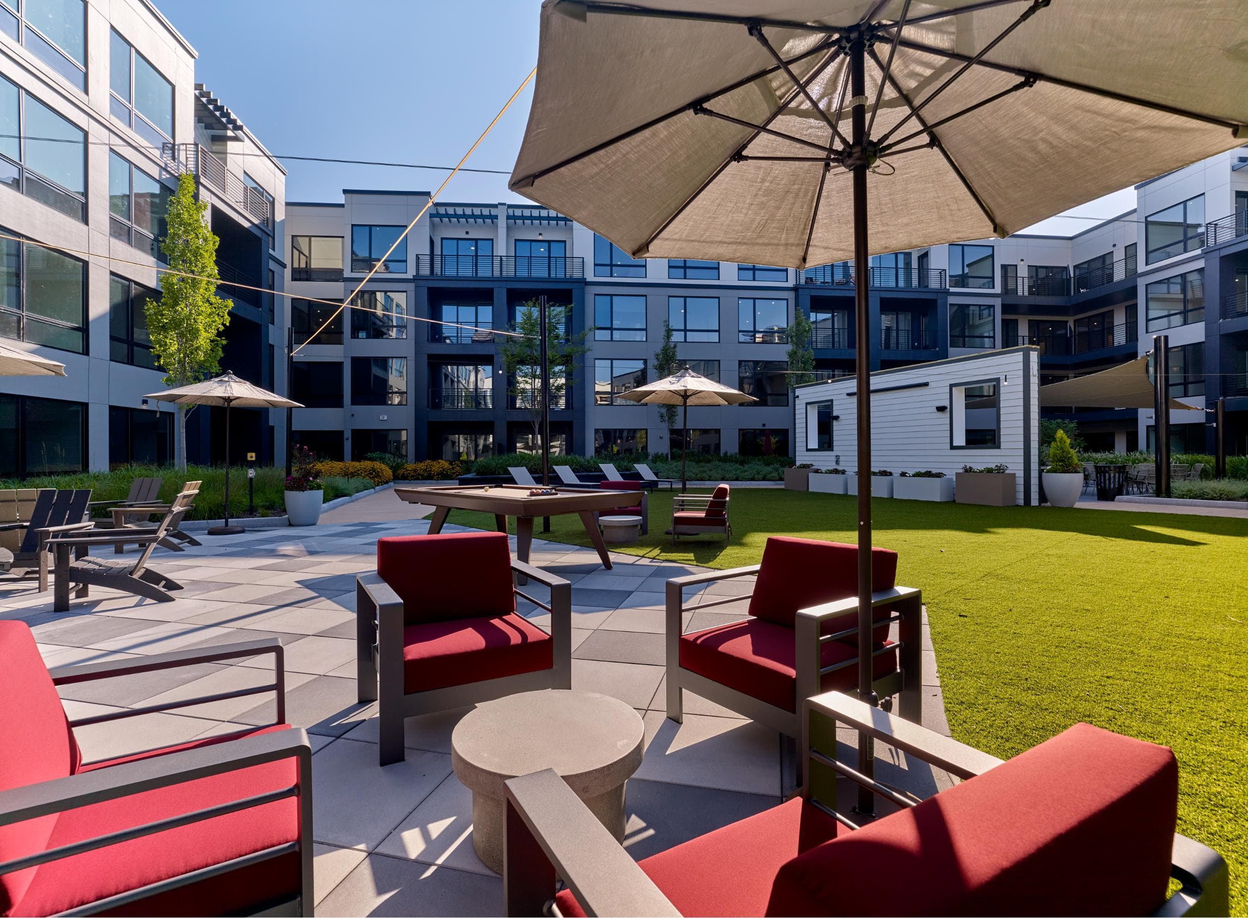 A patio with red chairs and a beige umbrella.