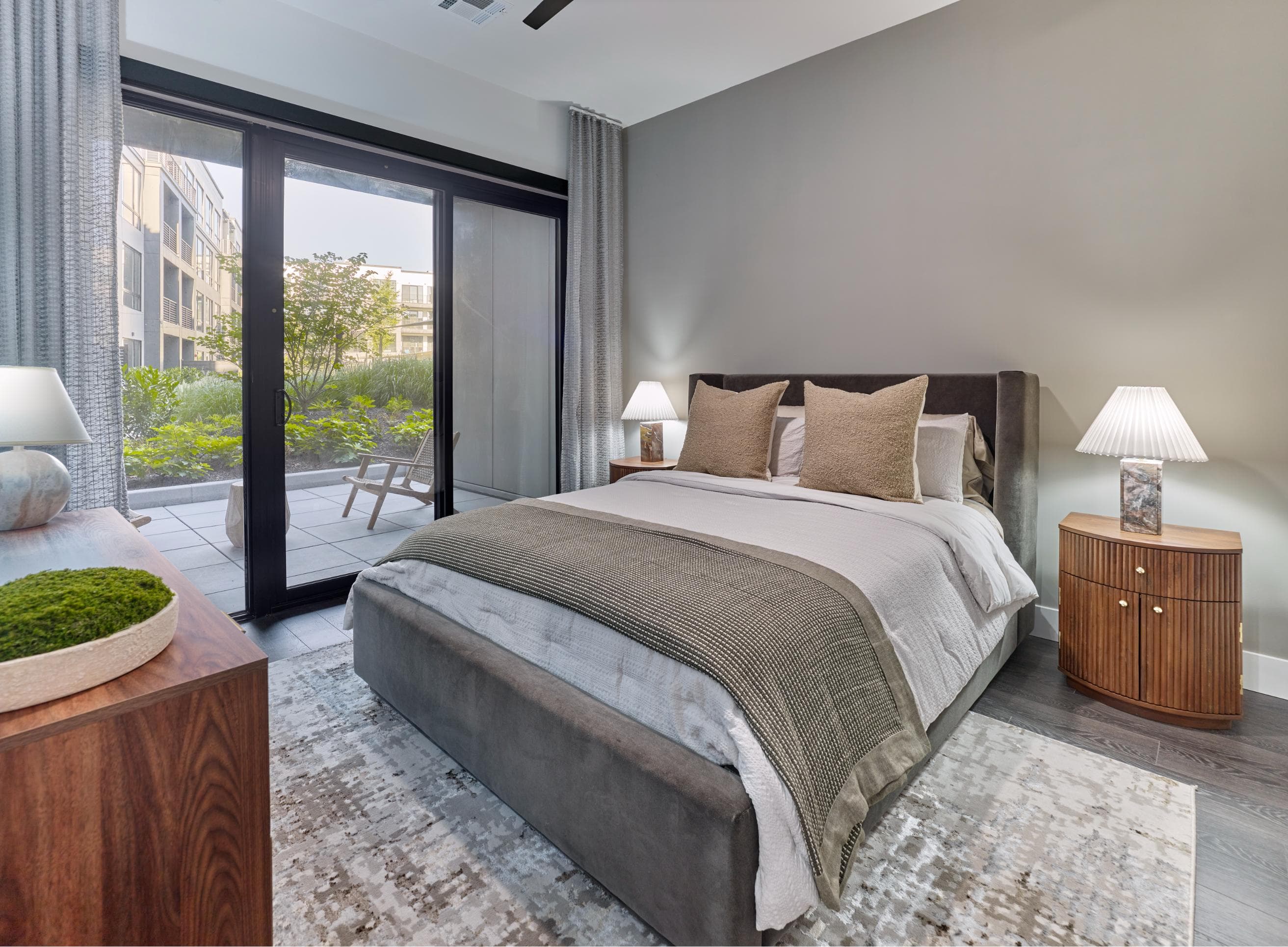 A bedroom with a large bed, a wooden nightstand, and a window with a view of the city.