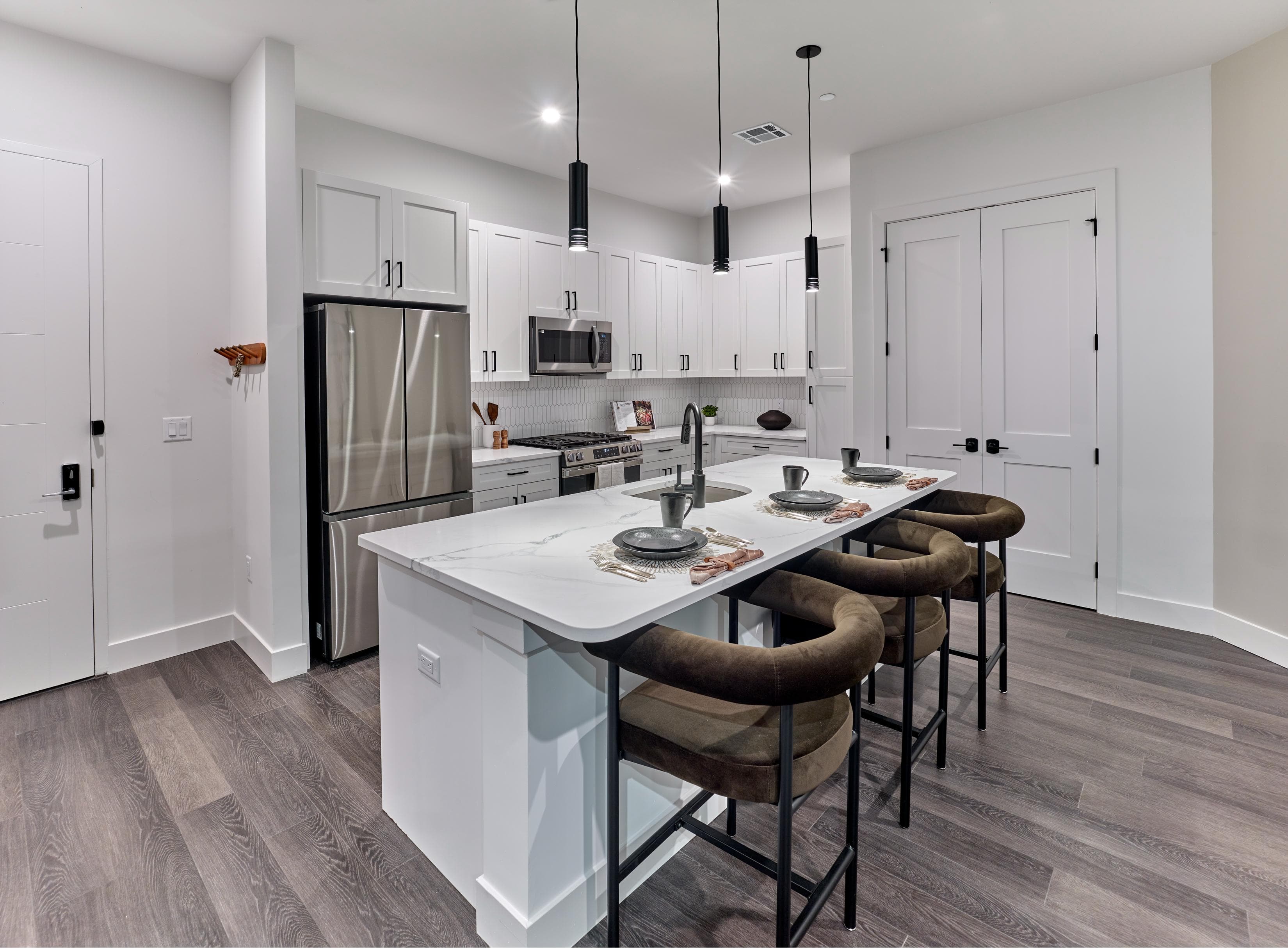 A modern kitchen with a white island and brown chairs.