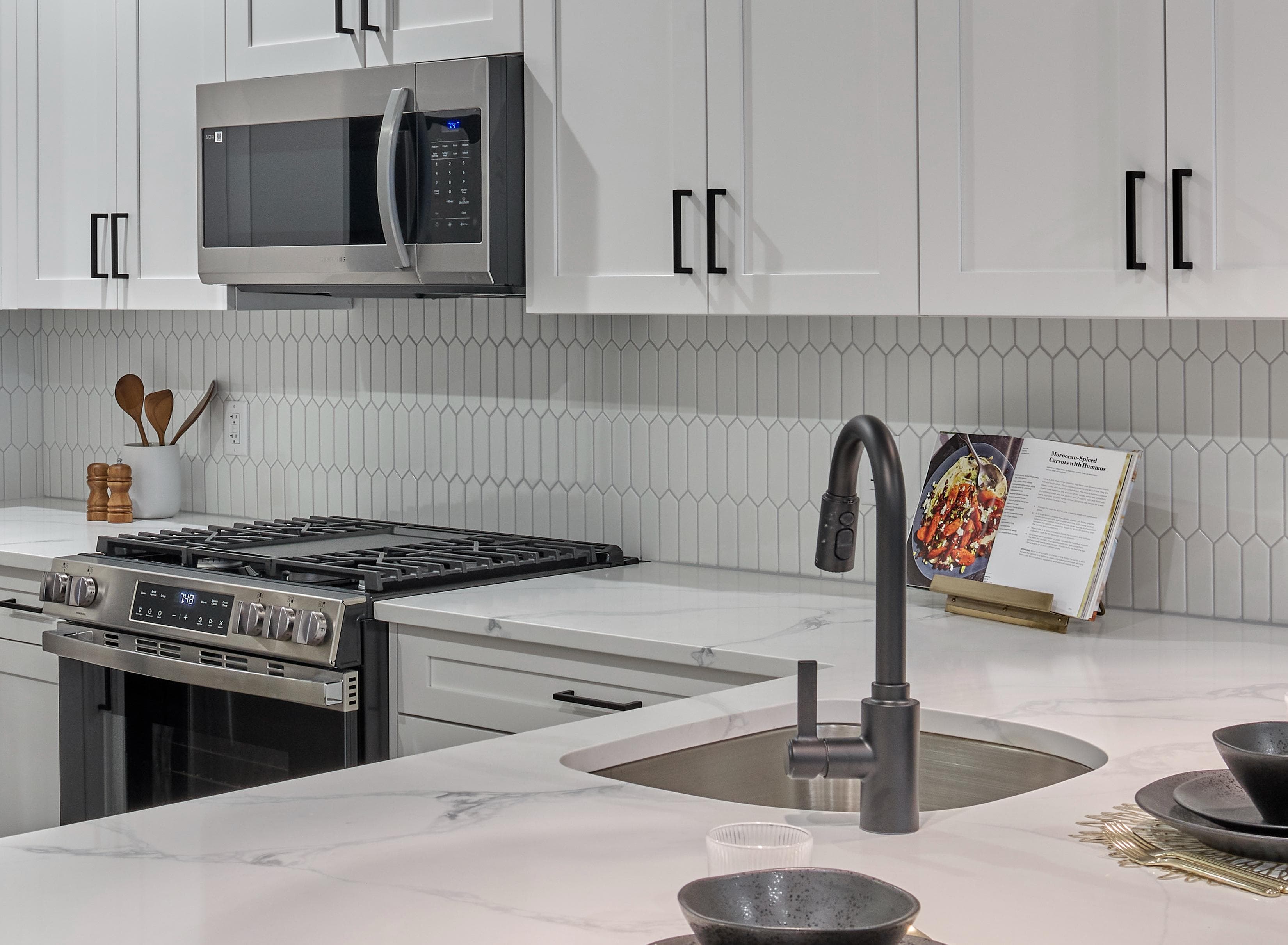 A modern kitchen with a stove, microwave, and white cabinets.