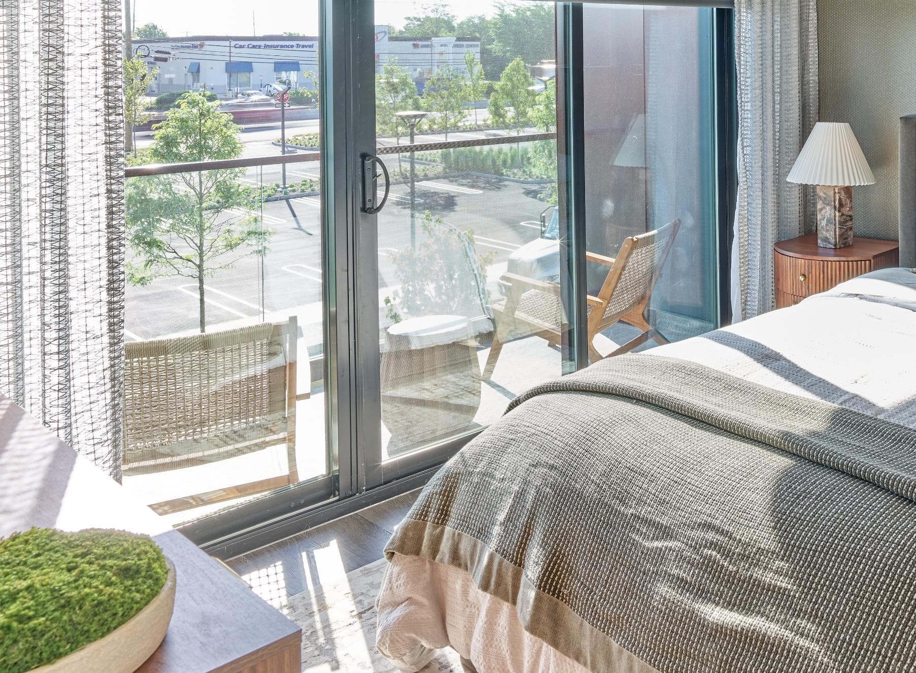 A bedroom with a large window overlooking a parking lot.