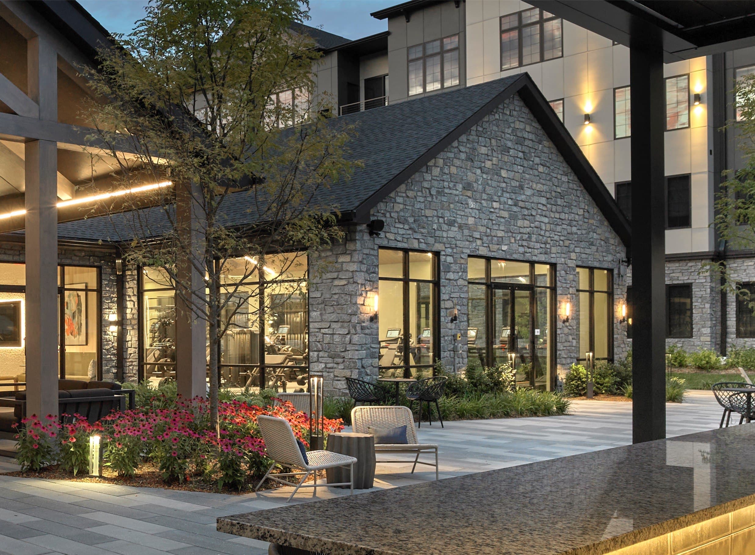 A stone building with a black roof is surrounded by a patio with chairs and a table.