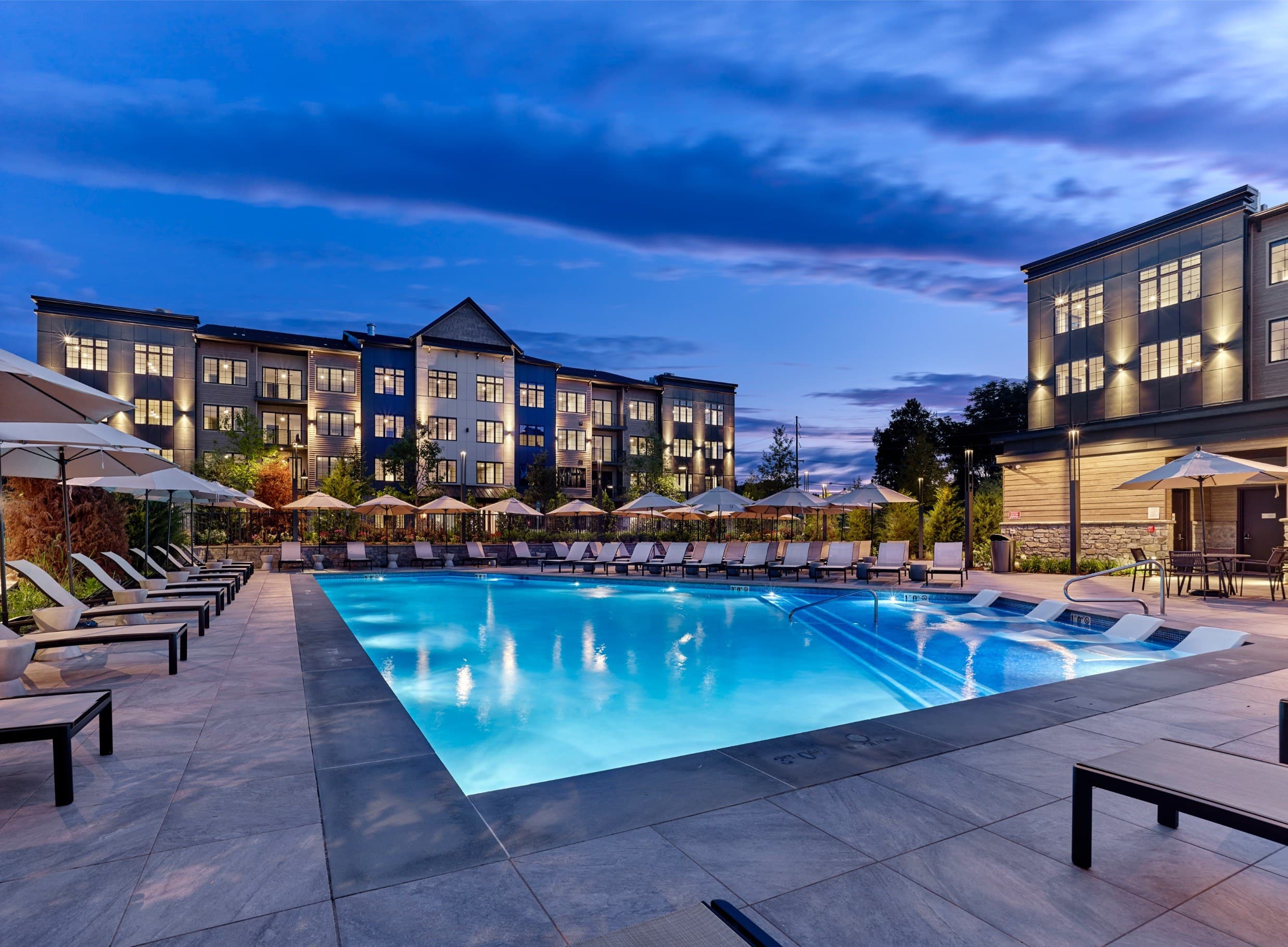 A large swimming pool surrounded by lounge chairs and umbrellas in front of a hotel.
